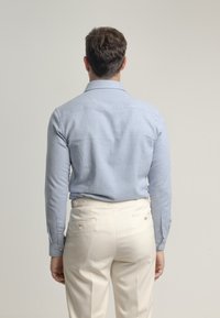 Camisa de manga larga azul claro con textura suave y puños abotonados, combinada con pantalones crema que cuentan con bolsillos traseros y botones.