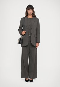 Completo grigio a righe sottili con un blazer su misura dotato di revers, abbinato a pantaloni a gamba larga. Gli accessori includono una piccola borsa nera.