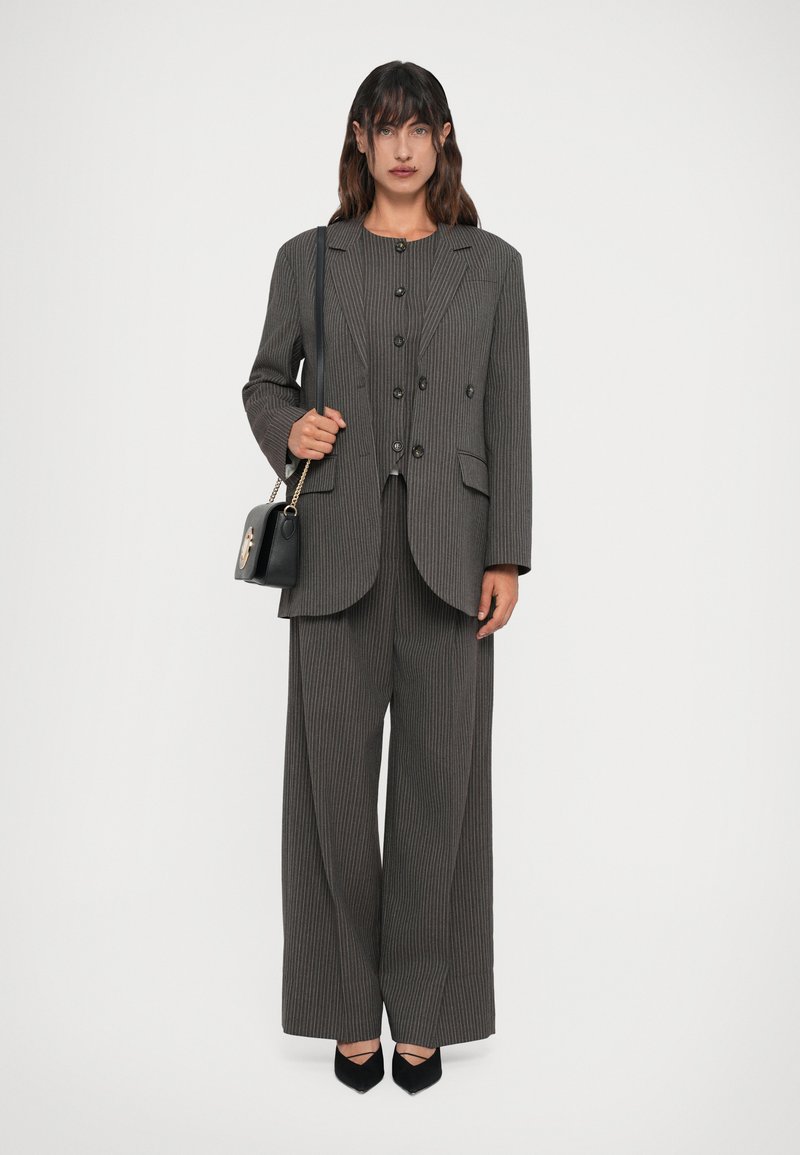 Completo grigio a righe sottili con un blazer su misura dotato di revers, abbinato a pantaloni a gamba larga. Gli accessori includono una piccola borsa nera.
