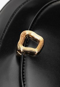 Czarna skórzana torba o gładkiej fakturze, z metalowym akcentem w złotym prostokącie z rowkami oraz szczegółowym przeszyciem wzdłuż krawędzi.