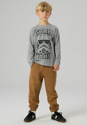 Graues langärmeliges T-Shirt mit einem schwarzen Stormtrooper-Aufdruck und dem Schriftzug "STAR WARS", kombiniert mit braunen Jogginghosen mit elastischen Bündchen.