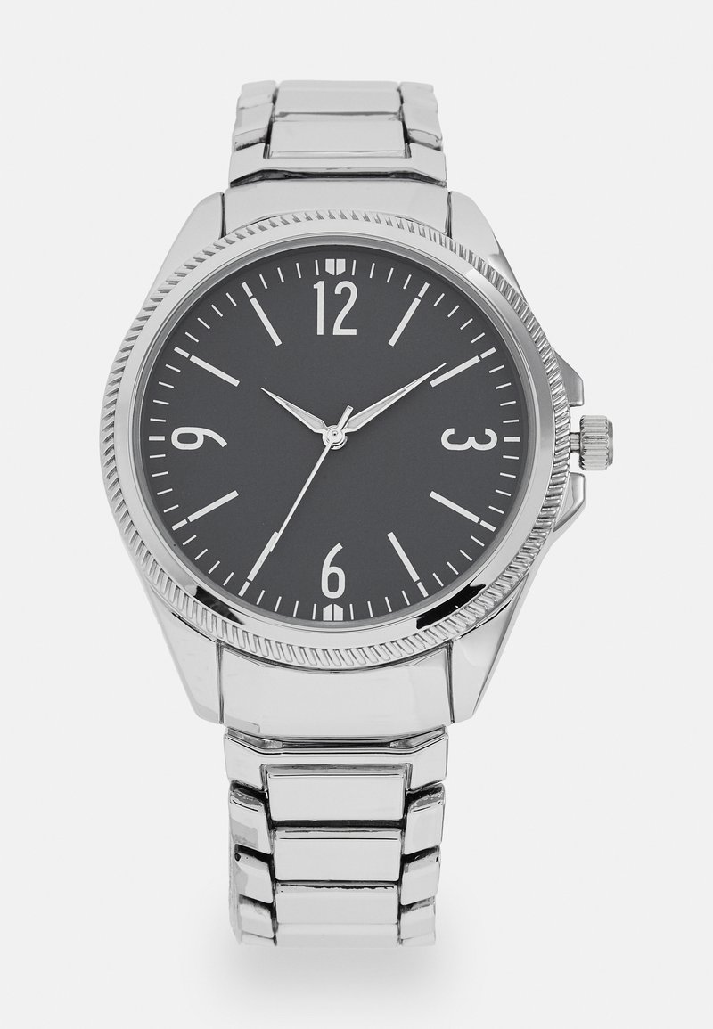 Montre analogique en argent avec un cadran noir, de grands chiffres blancs et un bracelet en acier inoxydable poli. Présente une lunette texturée et une couronne.