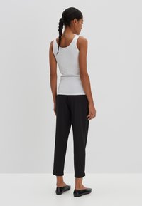 Witte mouwloze top gecombineerd met zwarte, tapse broek. Huidige stofstructuur, aansluitende vorm en eenvoudig ontwerp zonder zichtbare patronen of accenten.