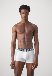 Baltas kokvilnas bokseris ar melnu Calvin Klein logotipa jostu. Dizains ir ar pieguļošu piegriezumu un gludu, mīkstu tekstūru.