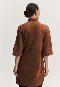 Bronzefarbenes langes Kleid aus weichem Wildleder mit Dreiviertelärmeln und leicht A-Linien-Form, mit glatter Oberfläche und ohne sichtbare Verschlüsse.
