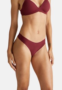 Haut de bikini bordeaux et bas taille basse en tissu lisse. Le haut présente un décolleté plongeant ; le bas offre une couverture minimale et un design sans coutures.