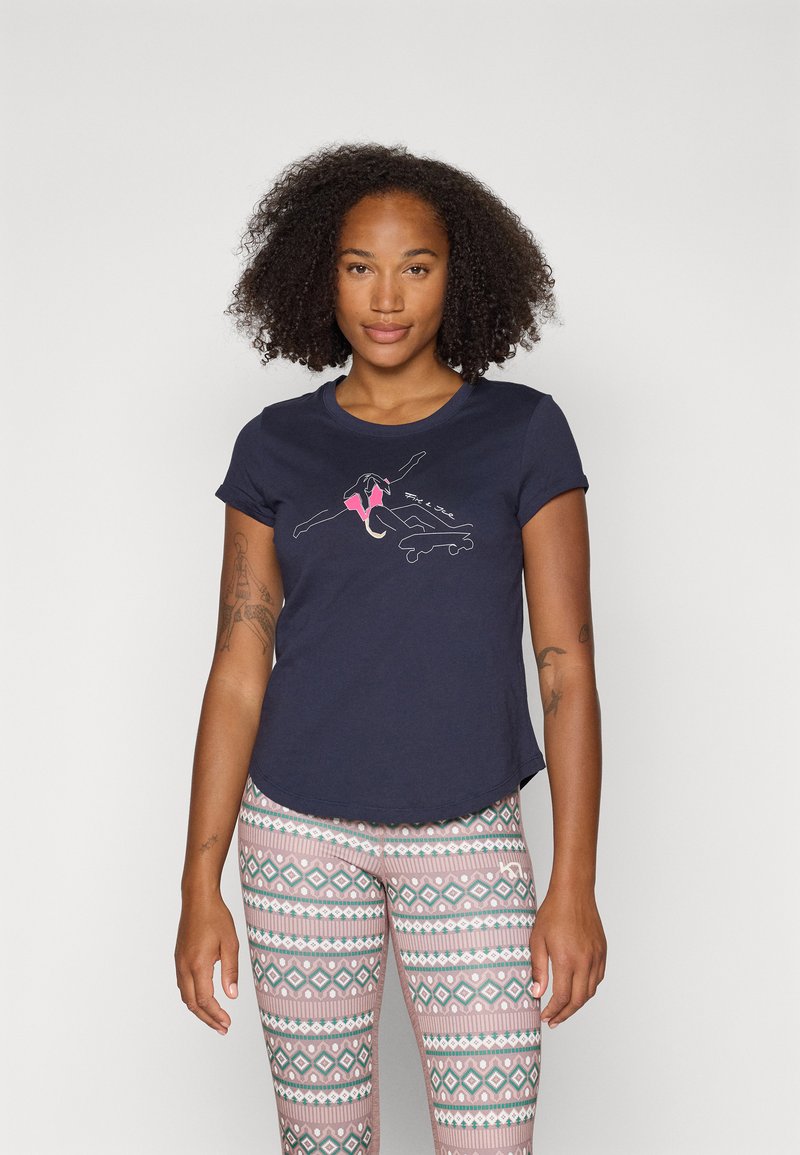 Marineblaues T-Shirt mit kurzen Ärmeln und einem Cartoon-Graphic in Pink und Weiß, kombiniert mit gemusterten Leggings in Pastellfarben mit geometrischen Designs.