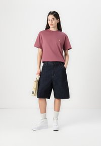 Passagerar blå t-shirt med korta ärmar och en liten logotyp, i kombination med mörka denimshorts och vita högmidjade sneakers.