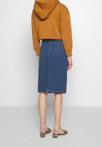 Denim midi skirt with a fitted waist and a smooth finish, paired with a mustard-colored hoodie and leopard print heeled mules.