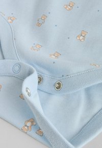 Lyseblåt bomuldskropssuit med gentaget bjørnemønster, rund halsudskæring og trykknapper i bunden. Blød, glat tekstur.