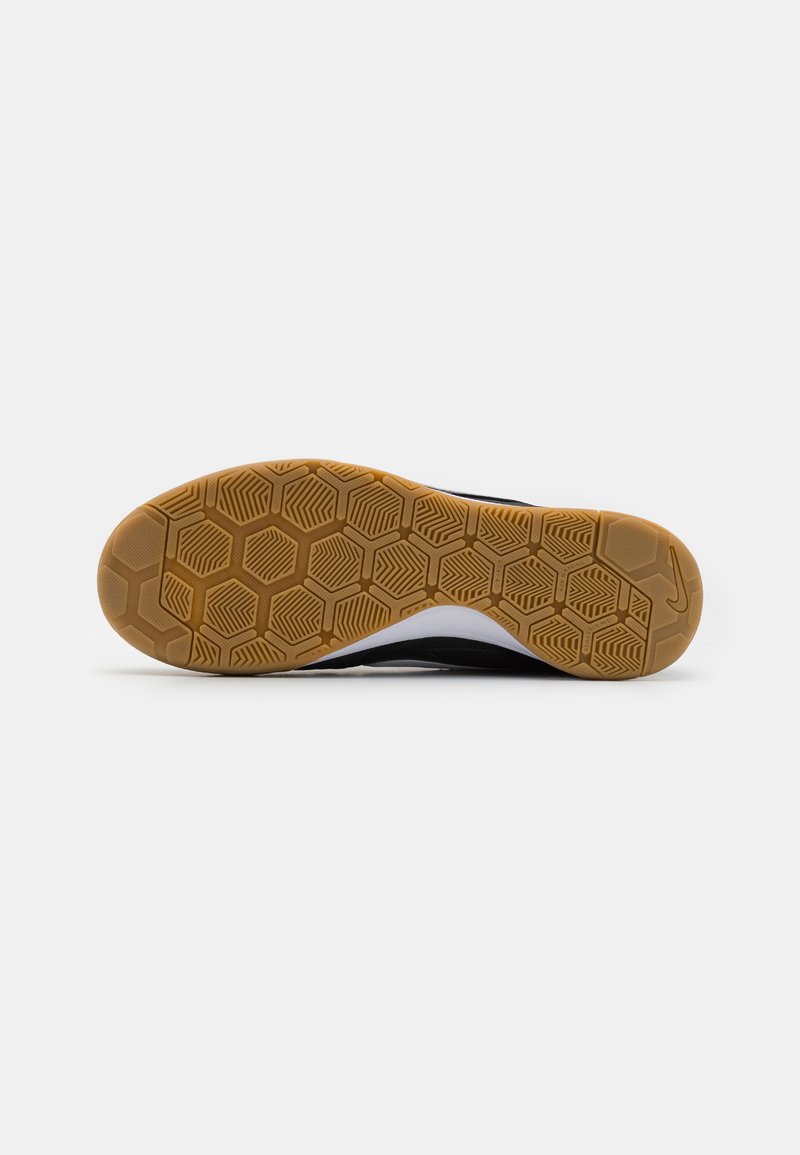 Semelle de chaussure de sport noire avec un motif en nid d'abeille, dotée d'une semelle extérieure en caoutchouc beige et d'accents blancs sur le côté.
