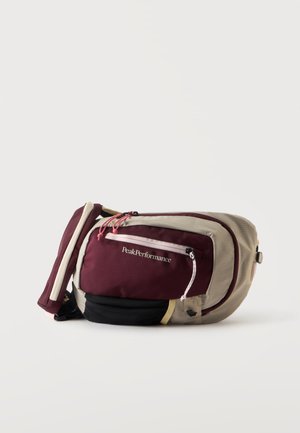 Sac banane compact avec sections beige, bordeaux et noir, poche avant zippée et logo "Peak Performance" sur le panneau bordeaux.