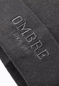 Grå stickad mössa med ett präglat "OMBRE"-logotyp och textilstruktur. Den har en tät passform, perfekt för värme och komfort.