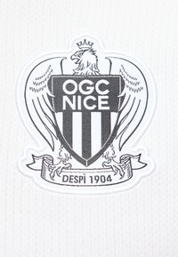 Blason en noir et blanc du club de football OGC Nice représentant un aigle avec une couronne et le texte "DESPI 1904" sur un fond en tissu blanc.
