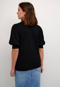 Black textured sweater with puffed sleeves. Soft, fitted design. Paired with a light blue denim skirt, showing a casual outfit combination.