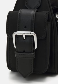 Mochila preta com um tecido mate, detalhes em pele e fecho de fivela prateada. Inclui um bolso com um detalhe de borda cosida.