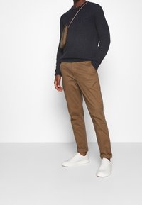 Marineblauwe gestructureerde gebreide trui, kaki chino's en witte sneakers, met een kleine bruine schoudertas. Casual outfit, slank silhouet.