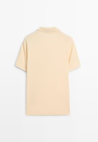 Polo beige à manches courtes, vu de dos, avec un col simple et sans logos ni motifs visibles.