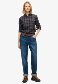 Checkered flannel shirt in navy, red, and yellow; classic fit. Pair of blue denim jeans, relaxed fit; brown leather boots with yellow laces.