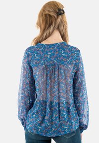 Blusa blu trasparente con motivo floreale, maniche lunghe, colletto rotondo, dettaglio plissettato sul retro e tessuto leggero. Abbinata a denim.