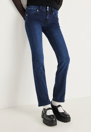 Pantalones vaqueros de mezclilla azul oscuro con pierna recta, que presentan costuras sutiles y dos bolsillos delanteros. Combinados con zapatos de plataforma negros y calcetines blancos.