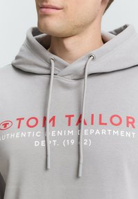 Hoodie gris en mélange de coton, avec une capuche à cordon, logo avant en rouge et blanc, et une coupe décontractée.