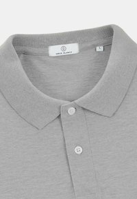 Polo-shirt gris clair en tissu doux, avec un col côtelé, trois boutons et une étiquette "SERGE BLANCO" à l'intérieur du cou.