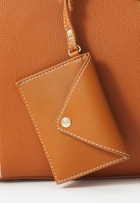 Borsa a mano in pelle marrone con finitura testurizzata, dotata di un portacarte abbinato attaccato tramite una tracolla, rifinita con cuciture bianche e un bottone a pressione dorato.