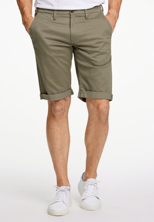 Olijfgroene katoenen shorts met omgerolde pijpen, zijzakken en een knoopsluiting, gecombineerd met witte sneakers.