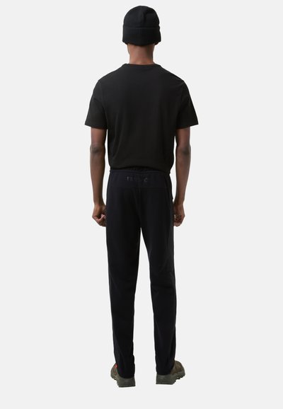 Sort kortærmet t-shirt parret med sorte sweatpants. Modellen bærer en sort beanie og vises fra bagenden. Behagelig pasform, afslappet stil.