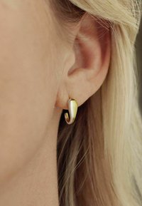 Pendientes de oro y plata con un diseño curvado y abstracto, que presentan una superficie lisa y un acento en espiral. Primer plano de la oreja.