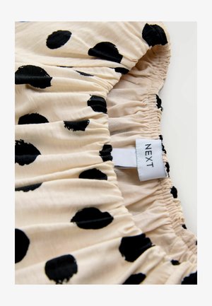 Tissu crème avec des pois noirs, présentant une texture froncée. L'étiquette indique "NEXT." Mise au point sur le motif imprimé et les détails de fronces élastiques.