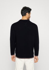 Maglione in maglia navy con maniche lunghe, scollatura rotonda e dettagli a strisce nel bordo contrastante, realizzato in tessuto morbido e testurizzato.