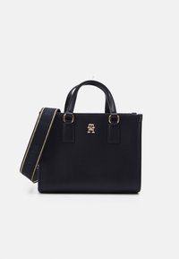 Svart lær tote bag med gull hardware, doble håndtak og avtakbar skulderrem med en merkevarelogo foran.