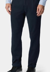 Granatowe spodnie uszyte z gładkiego materiału, o dopasowanym kroju, z bocznymi kieszeniami i mankietami. W połączeniu z czarnymi sneakerami.