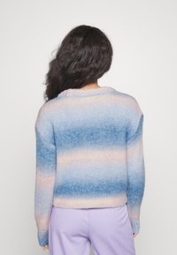 Pull en tricot avec un motif dégradé en bleu et pêche pastel, doté d'un col rond et d'une coupe décontractée. Complété par un pantalon lavande.