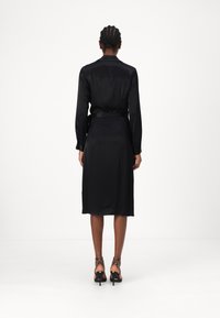 Black satin dress with long sleeves, a belted waist, and a knee-length hemline. Features a smooth texture and simple design without embellishments.