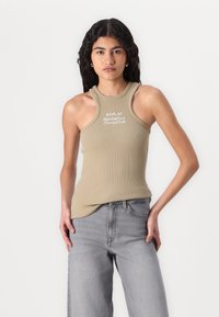 Ribbed khaki tielko s vysokým výstrihom a vyrezanými ramenami. Obsahuje biele nápisy "REPLAY Monte Carlo Bunny Club". Kombinované s svetlo šedými nohavicami.