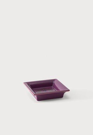 Square purple ceramic dish with a decorative floral wreath design inside, placed on a plain light background.