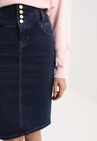 Denim blyertkjol i mörkblått, med hög midja och fem knappar, stickade detaljer och en figurnära silhuett.