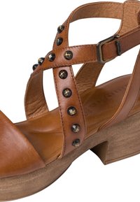 Bruna lädersandaler med korsade remmar, svarta nitar, en vadderad sula och en kraftig träklack.