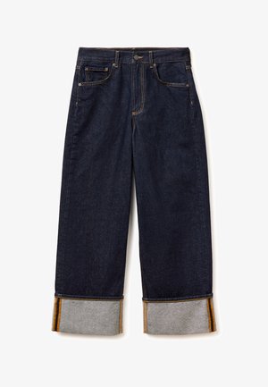 Jeans de mezclilla azul oscuro de pierna ancha con dobladillos remangados que muestran un tejido interior de rayas grises y naranjas.