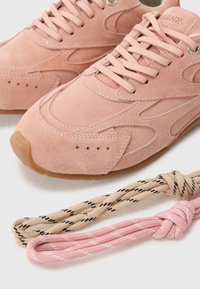 Baskets en suède rose clair avec des accents texturés sur les côtés et des lacets plats. Comprend deux options de lacets : beige avec un motif noir et rose uni.