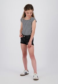 Stribede sort og hvid tætsiddende top med korte ærmer, parret med sorte denimshorts. Modellen har hvide sneakers med sorte detaljer på.