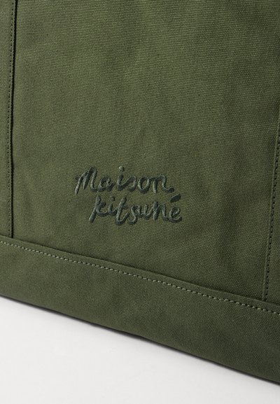 Roheline kangaskott, millel on tekstuurne pind, omab tumesinisest niidist brodeeritud „Maison Kitsuné“ logo, millele lisavad särtsu kontrastsed õmblused.