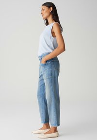 Lichtblauwe mouwloze top, ontspannen pasvorm. Gecombineerd met lichtgewassen spijkerbroek met zakken en gestikte details. Beige ballet flats.