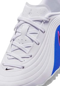 Bijela sportska cipela s bijelim vezicama, plavom teksturiranom bočnom stranom, ružičastim detaljem s logotipom i crnim Nikeovim znakom blizu prsta.