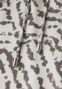 Tessuto leggero con un motivo astratto in nero e grigio. Presenta due cordoncini con punte metalliche per la regolazione.