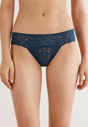 Marineblauwe kanten string met bloemenpatronen, doorschijnende delen en een brede kanten tailleband. Zachte textuur met scalloped randen.
