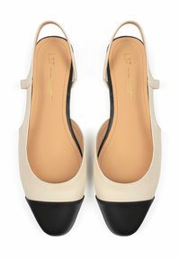 Scarpe slingback in pelle beige con punte in vernice nera. Texture liscia, lati aperti e tacco basso, con una forma arrotondata.